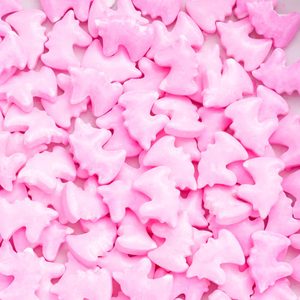 Pink candy pieces shaped like dinosaurs are scattered across a flat surface, creating a playful and colorful scene.