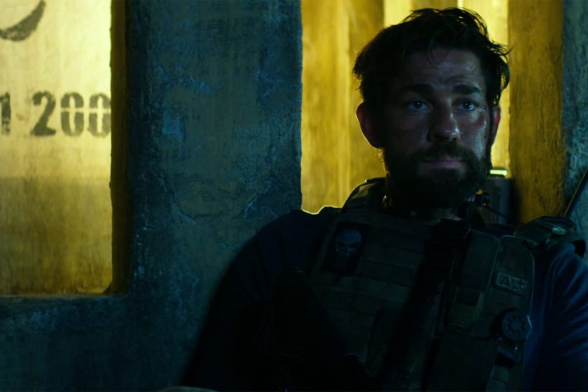 A man with tactical gear sits against a wall, looking contemplative. Yellow light and graffiti-like markings create a tense atmosphere.
