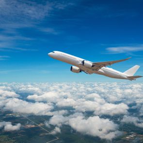 Airplane soars skyward above fluffy clouds, under a bright blue sky.