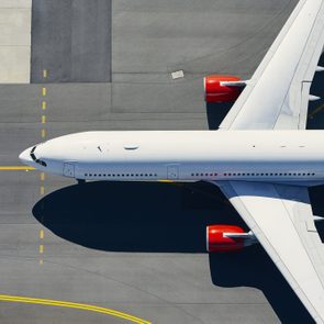 Airplane taxiing on a runway, showing top view with red engines, surrounded by gray tarmac and yellow guidance lines.