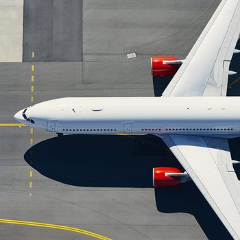 Airplane taxiing on a runway, showing top view with red engines, surrounded by gray tarmac and yellow guidance lines.