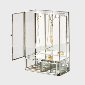 Glass jewelry box displays necklaces and rings, showcased in open compartments, against a plain gray background.