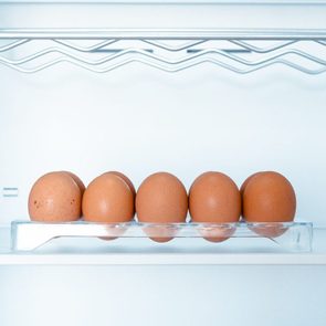 Six brown eggs sit in a clear tray inside a bright white refrigerator.