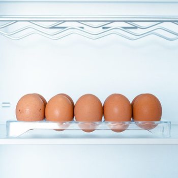 Six brown eggs sit in a clear tray inside a bright white refrigerator.