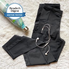 Black leggings lie on a textured surface with white earbuds placed on them. A patterned water bottle is nearby. Text: 