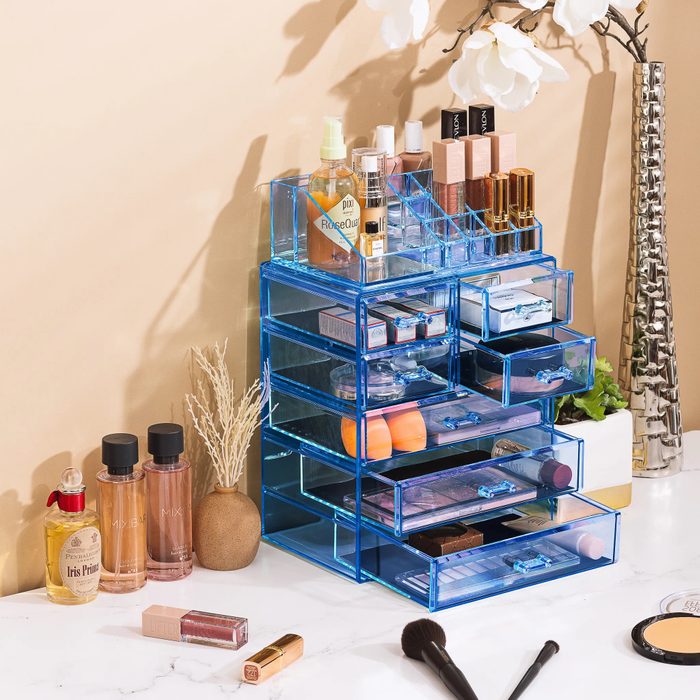 Organizer holds makeup products, displayed neatly on a vanity with decorative items, brushes, and few bottles around, creating a tidy and stylish setting.