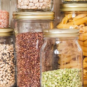 Jars hold various dry foods, like pasta and beans, arranged neatly on wooden shelves.