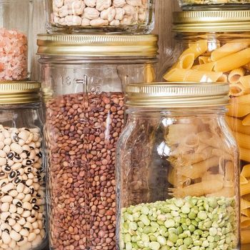 Jars hold various dry foods, like pasta and beans, arranged neatly on wooden shelves.