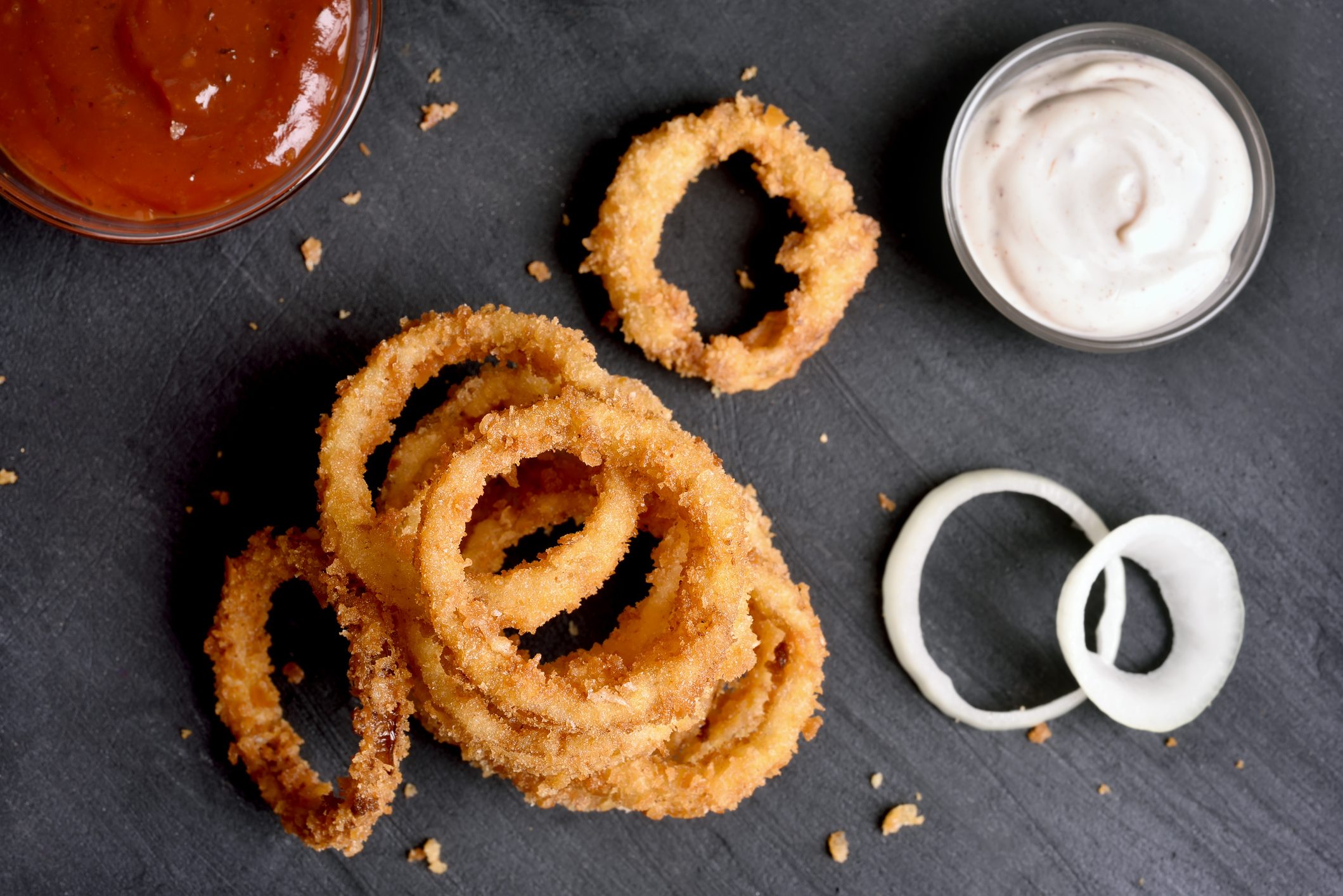 Fried onion rings with sauce on black stone background