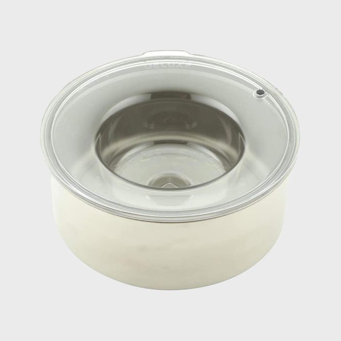Metallic ice cream maker bowl with clear lid sits against a plain background.