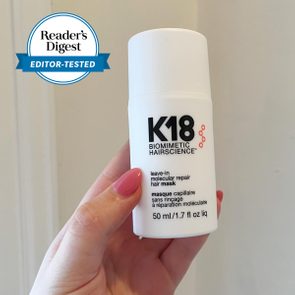 Hand holds white K18 hair mask bottle; blue 