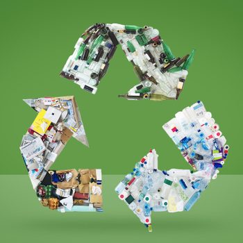 Recycling symbol formed by various recyclables; cardboard, glass, plastic; on a green background.