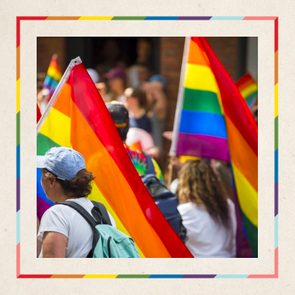 People carry rainbow flags at an outdoor event, surrounded by other participants in a festive atmosphere.