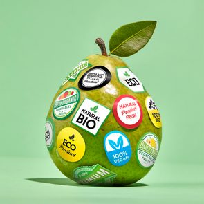 A pear covered in stickers promoting organic, vegan, and eco-friendly qualities sits on a green background.