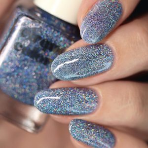 Glittery blue nails shine, reflecting light, held near matching nail polish bottle in a close-up view.