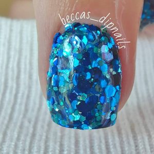 Blue glitter-covered fingernail sparkles under light, surrounded by a knit fabric background. Text reads 