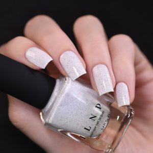 Hand holds a bottle of white nail polish with colorful speckles, nails painted to match, against a black background.