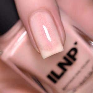 Fingernail displays shimmering, light pink nail polish; background shows a blurred nail polish bottle labeled 