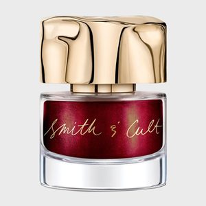 A nail polish bottle sits with a wavy gold cap, labeled 