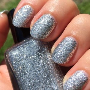 Fingers display sparkling silver nail polish, holding a matching glitter bottle, in bright natural light.