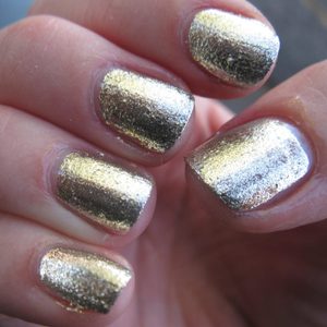 Fingernails adorned with metallic gold polish, held closely, reflecting light in a natural setting.