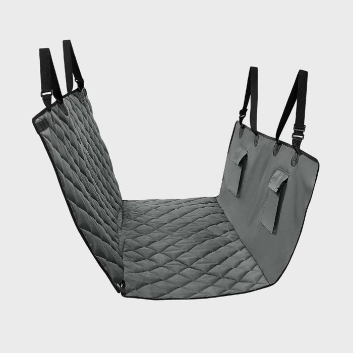Quilted pet seat cover suspended with straps, positioned for use in a car, displaying a gray padded surface and storage pockets.