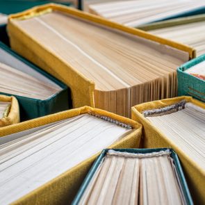 Books lie stacked closely, displaying worn pages and colorful cloth covers, suggesting an old library or collection setting.