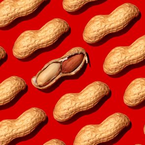 Peanuts scattered on red background; one cracked open revealing two differently colored nuts inside.