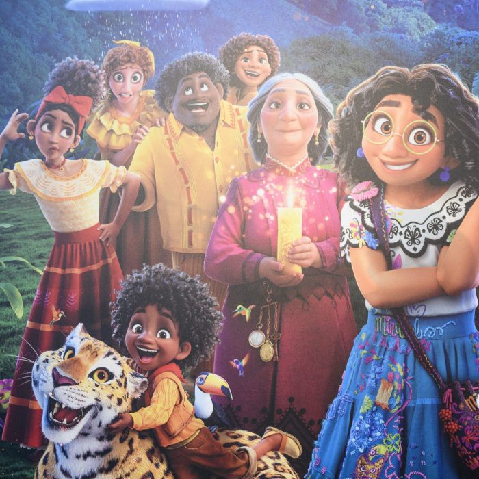 Animated characters smile and pose together in a lush landscape; a child hugs a jaguar while a person holds a glowing candle.