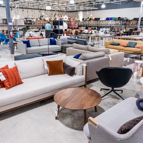 Furniture showroom displays various sofas and chairs; surrounding area includes tables and lighting fixtures in a well-lit, spacious interior with polished concrete floor.