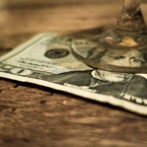 A glass rests on a twenty-dollar bill, situated on a wooden surface.
