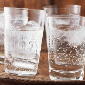 Glasses filled with sparkling water and ice stand on a wooden tray, creating a refreshing scene indoors.