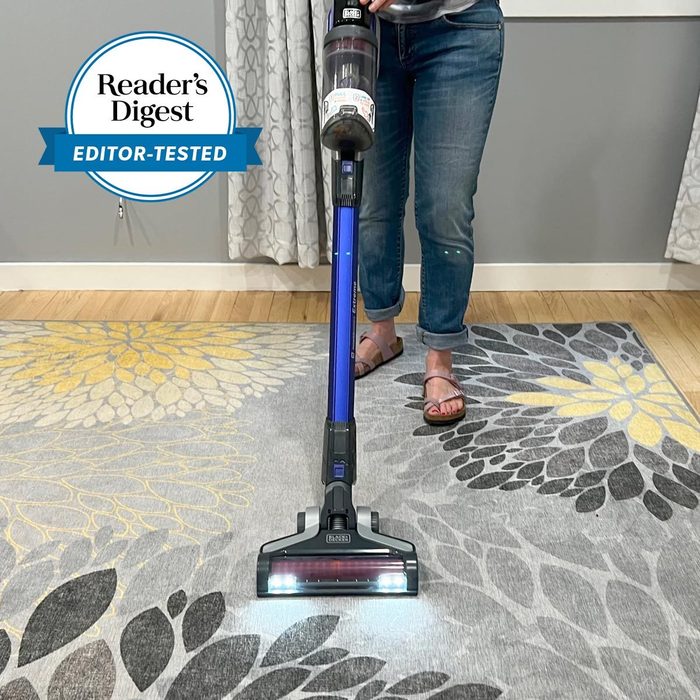Vacuum cleaner moves over floral-patterned rug; person in jeans guides it. Badge: 