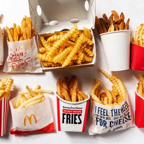 Various fast-food fries are displayed in containers on a white surface, featuring brands like Burger King, McDonald's, KFC, and Chick-fil-A.