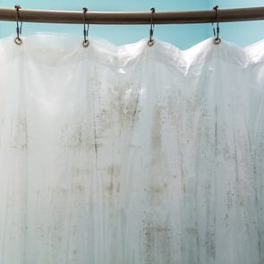 Shower curtain hangs with mold spots on its surface, set against a light blue bathroom wall.