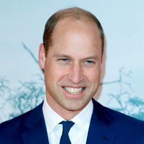 Man smiling, wearing a suit and tie, against a light blue background with faint outlines of branches.
