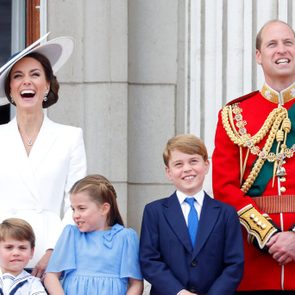 Group poses joyfully; adults in formal attire, children in blue outfits, standing on balcony with decorative columns behind them.