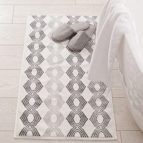 Slippers rest on patterned rug beside white bathtub in a bright, tiled bathroom setting.
