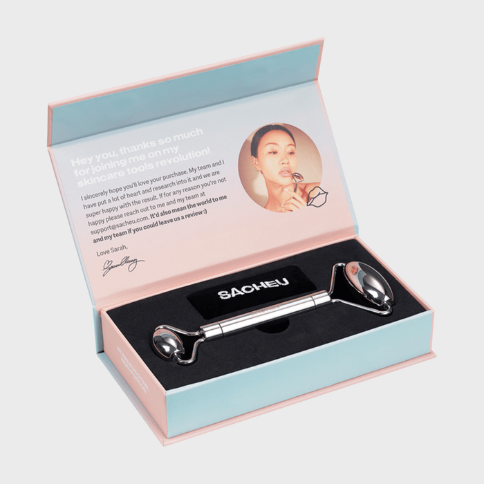 Facial roller rests inside an open pastel-colored box with an appreciative note and image inside the lid. The box displays the brand 