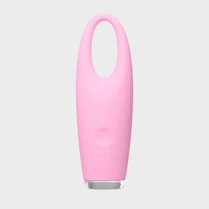 A pink silicone eye massager stands upright with a loop handle, buttons visible, on a plain gray background. Text: 
