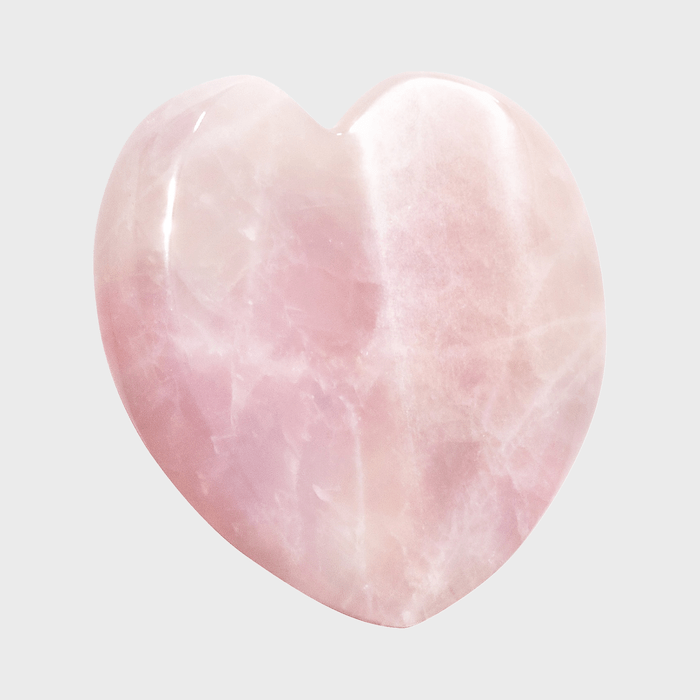 A polished rose quartz heart sits against a plain, light gray background.