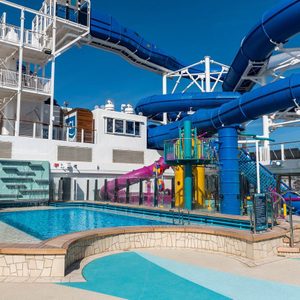 Water slides twist over a cruise ship's deck, surrounded by pools and bright play structures, under a clear blue sky.