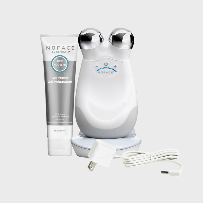 Facial toning device sits beside gel primer and charging cable, set on a plain surface.
