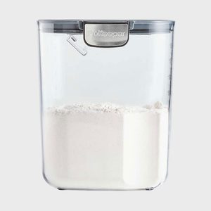 A translucent container filled with white flour sits against a plain background, displaying the label 