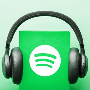 Headphones rest on a green notebook displaying the Spotify logo, set against a light green background.