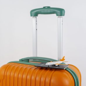 An orange suitcase supports a miniature airplane and passport, set against a plain background.