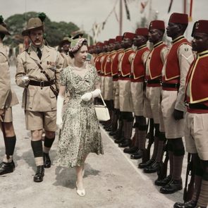 A woman in a floral dress walks past uniformed soldiers during a formal military parade outdoors.