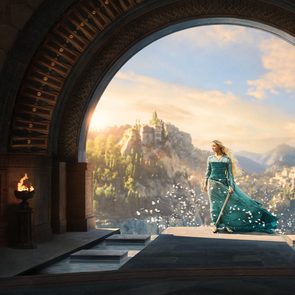 A figure in a flowing teal dress stands with a sword in hand, framed by an archway overlooking a sunlit, mountainous landscape.