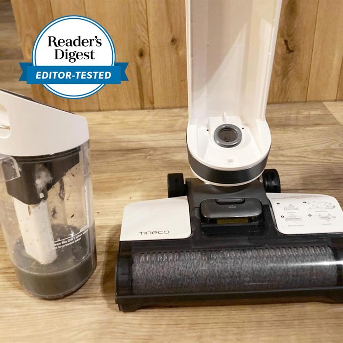 Vacuum cleaner sits disassembled on wooden floor with dust container beside it, showcasing 