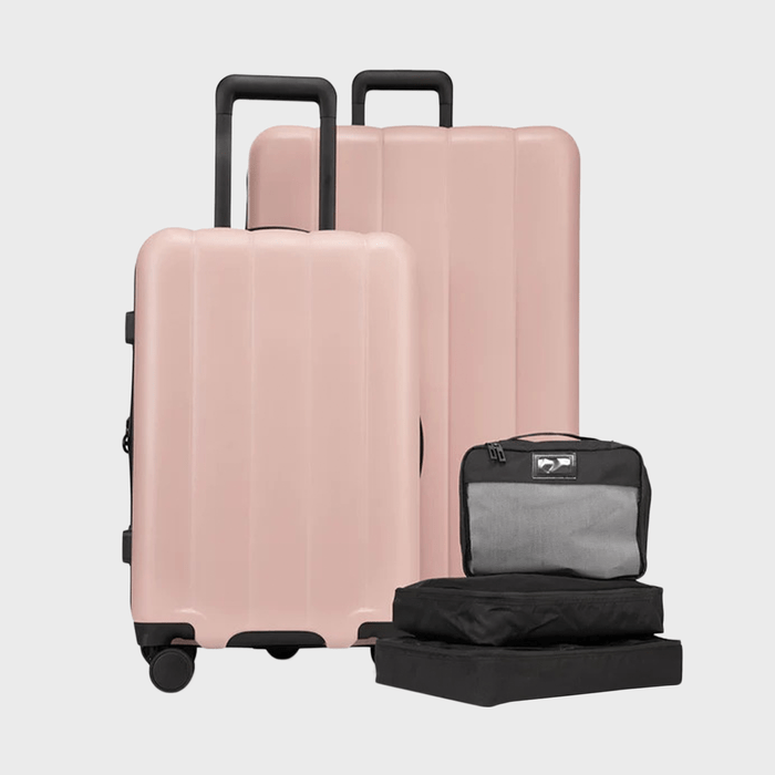 Two pink suitcases with extended handles stand upright; next to them are three black packing cubes. All against a plain, light background.